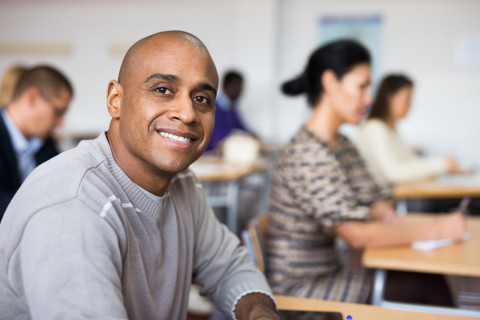 Homme avec un sourire fière et paisible, installé dans une salle de cours au milieu d'autres apprenants adultes